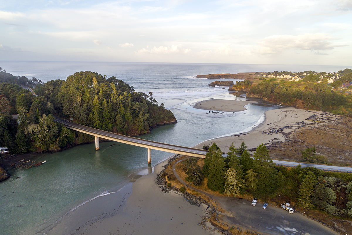 A highway over a river that opens to the ocean with forest on either side of the bridge