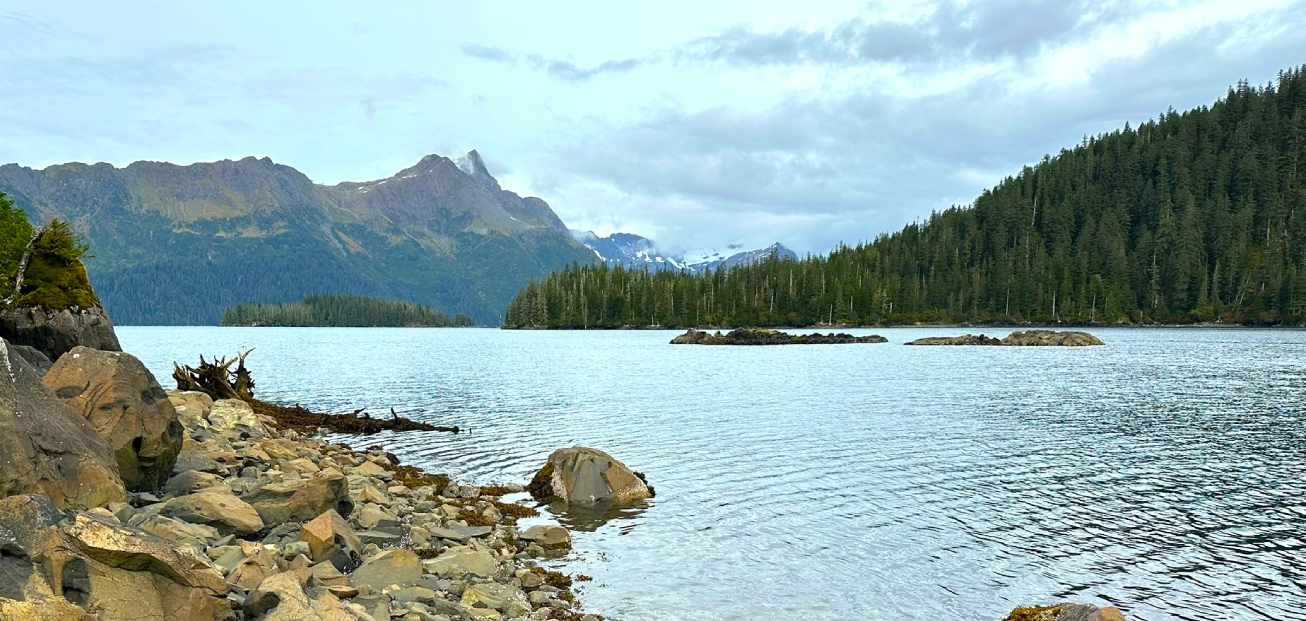 Scenic view of Herring Pete's Cove on Nuka Island, featuring a tranquil lake surrounded by rocks and lush trees.
