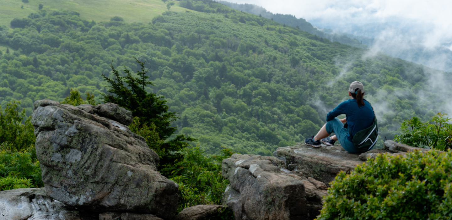 The back of a woman taking a break after hiking with lush, green landscape ahead of her gaze