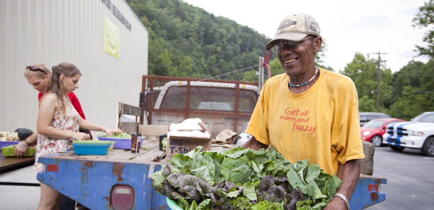 A smiling man delivers green, leafy vegetables out of the bed of his old truck