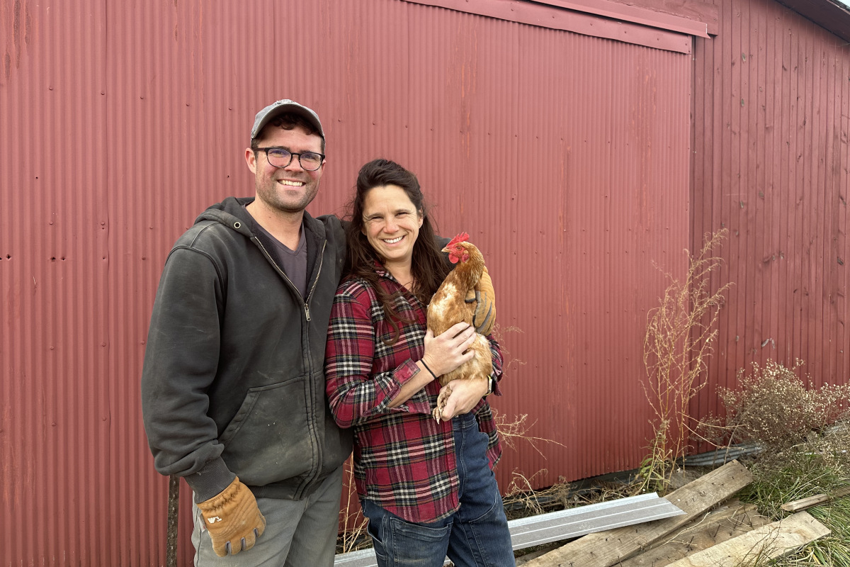 The owners of Kakadoodle Farm, one of The Conservation Fund's Farms Fund farms, pose with a hen in front of a red barn.