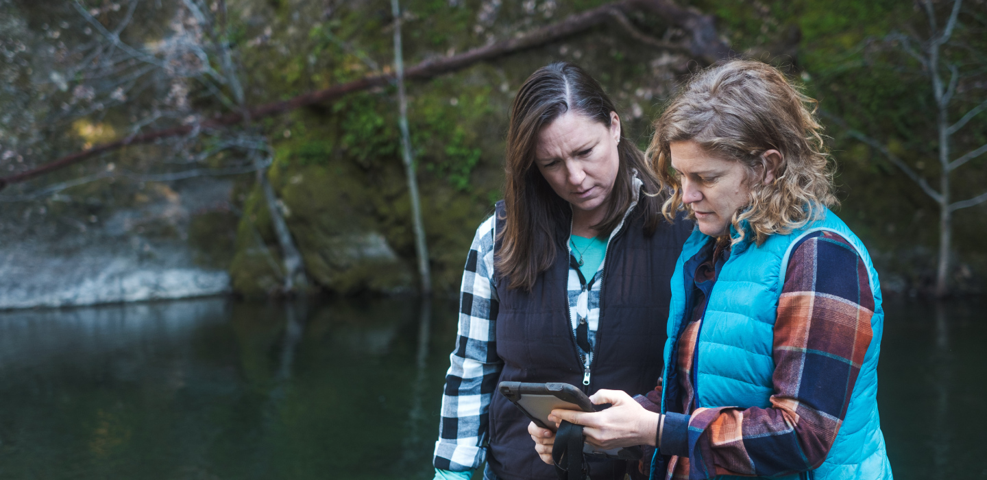 Two women looking at a device next to a body of water in Northern California
