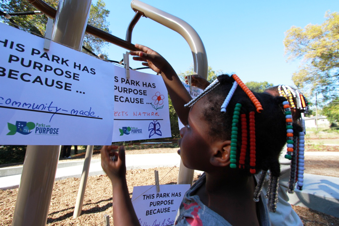 A young girl hangs a sign detailing why parks have purpose next to similar signs