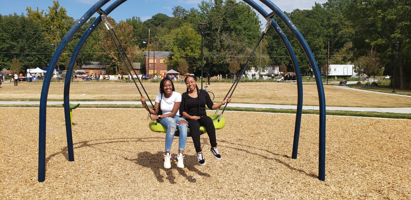 Two smiling girls sitting on a swing at a playground