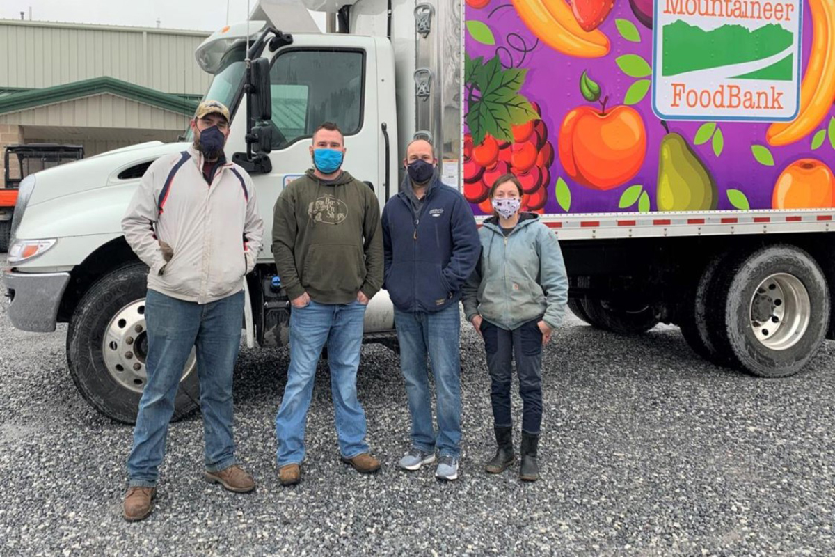 Four individuals from the Freshwater Institute stand in front of a Mountaineer Food Bank delivery truck. The three on the left are male and the one on the right is female. They are all wearing sweatshirts and jeans and masks due to the Covid pandemic.