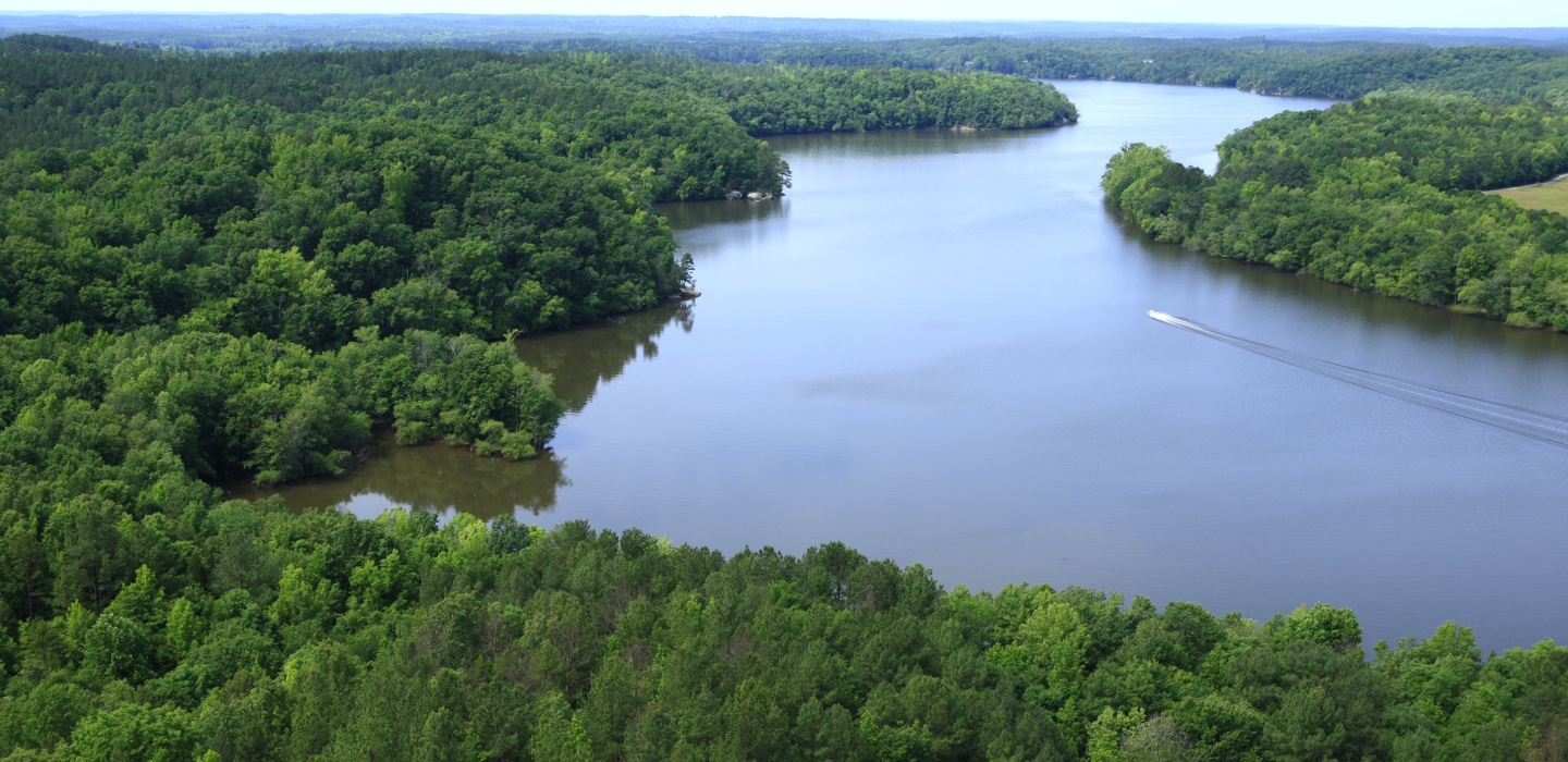 A single boat makes it was down a river winding between lush, green trees at Liberty Hill
