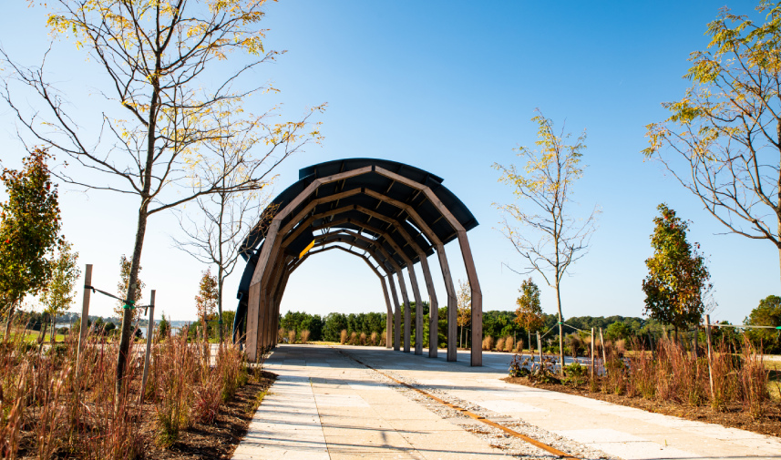 A covered walkway winds its way through young trees at Machicomoco State Park on a clear day