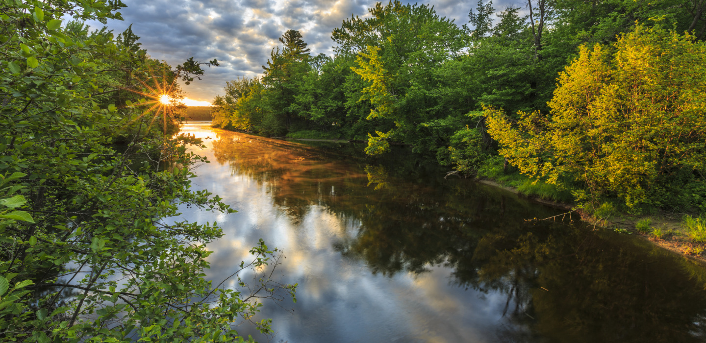 The sun shines onto Pleasant River as it sets on a summer day