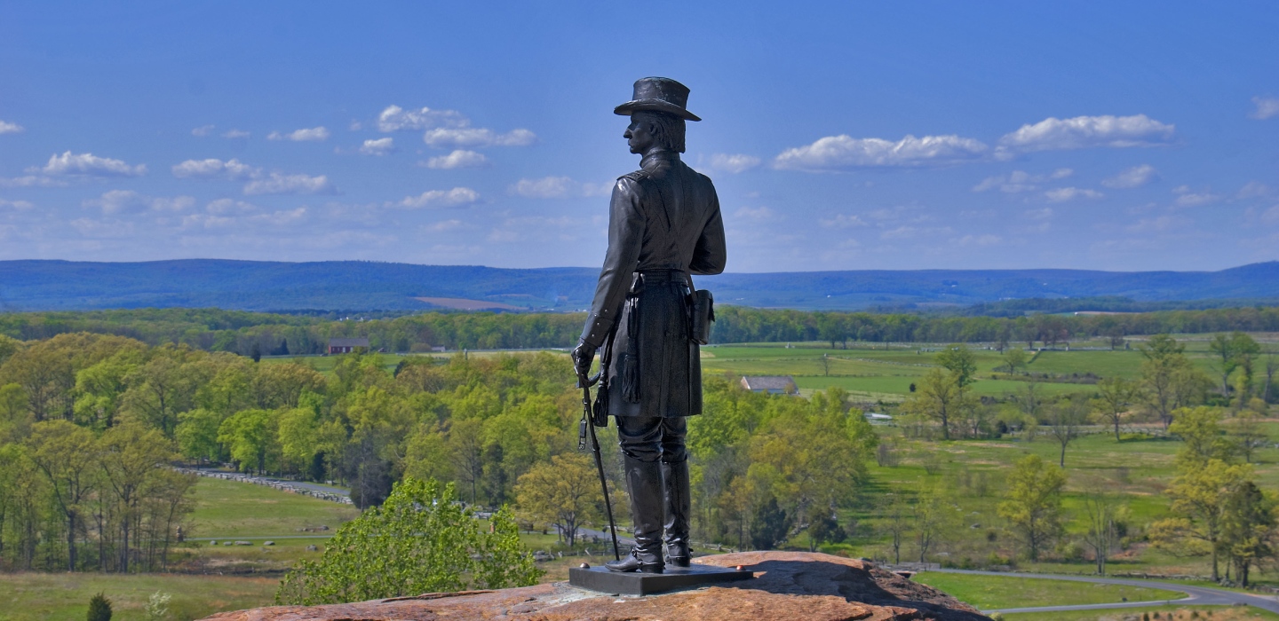 A statue at the Gettysburg National Military Park in Pennsylvania looks over a lush green landscape and mountains in the distance