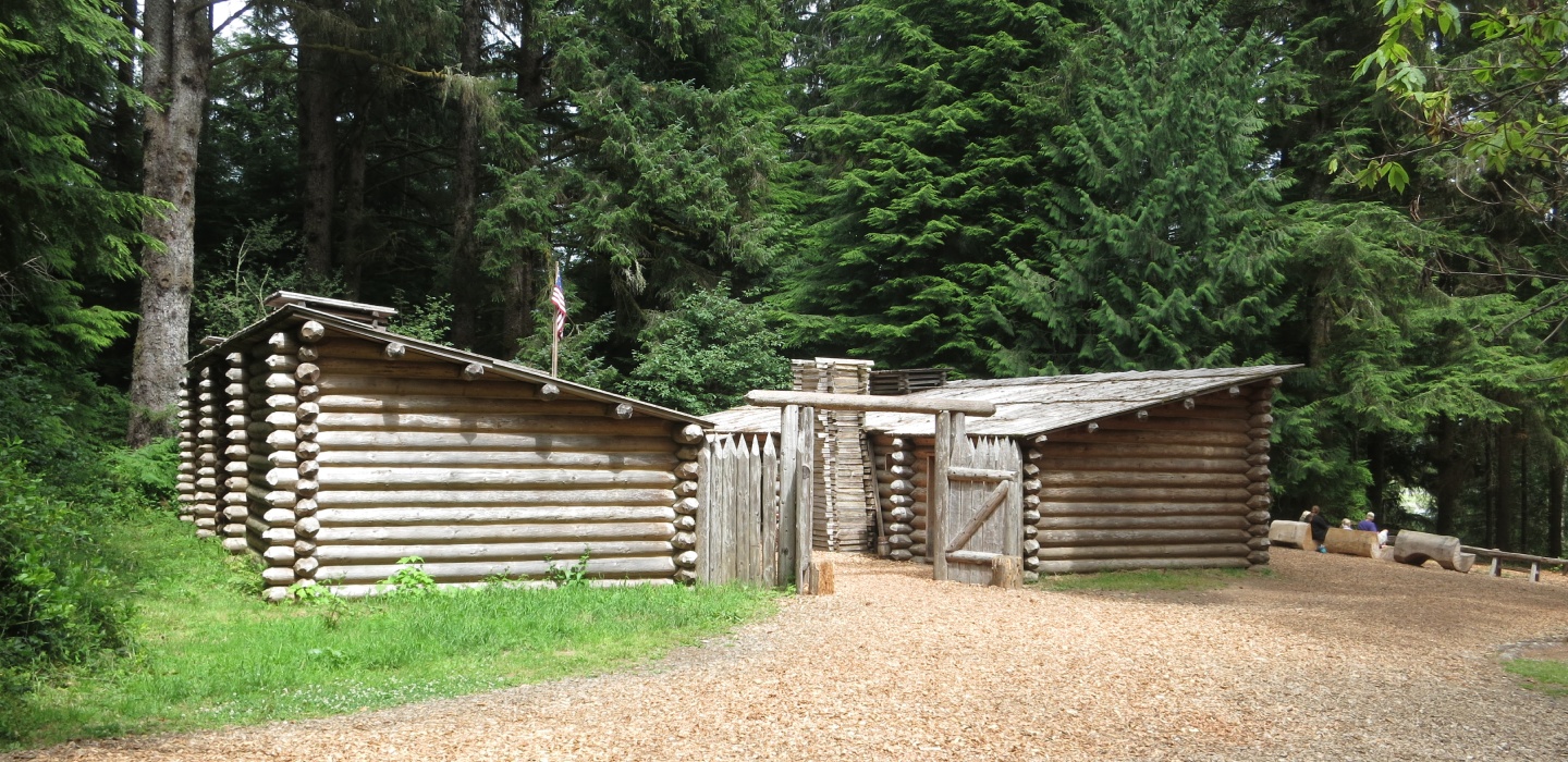 Two log cabins at the Lewis and Clark National Historical Park with greens trees in the background.