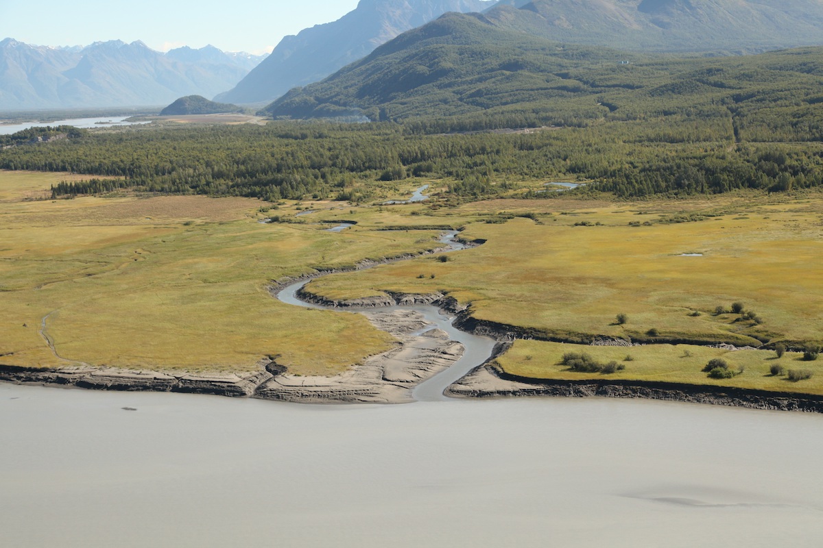 Mountains are the backdrop for a river winding through green lands on its way to the sea in Eklutna, Alaska.