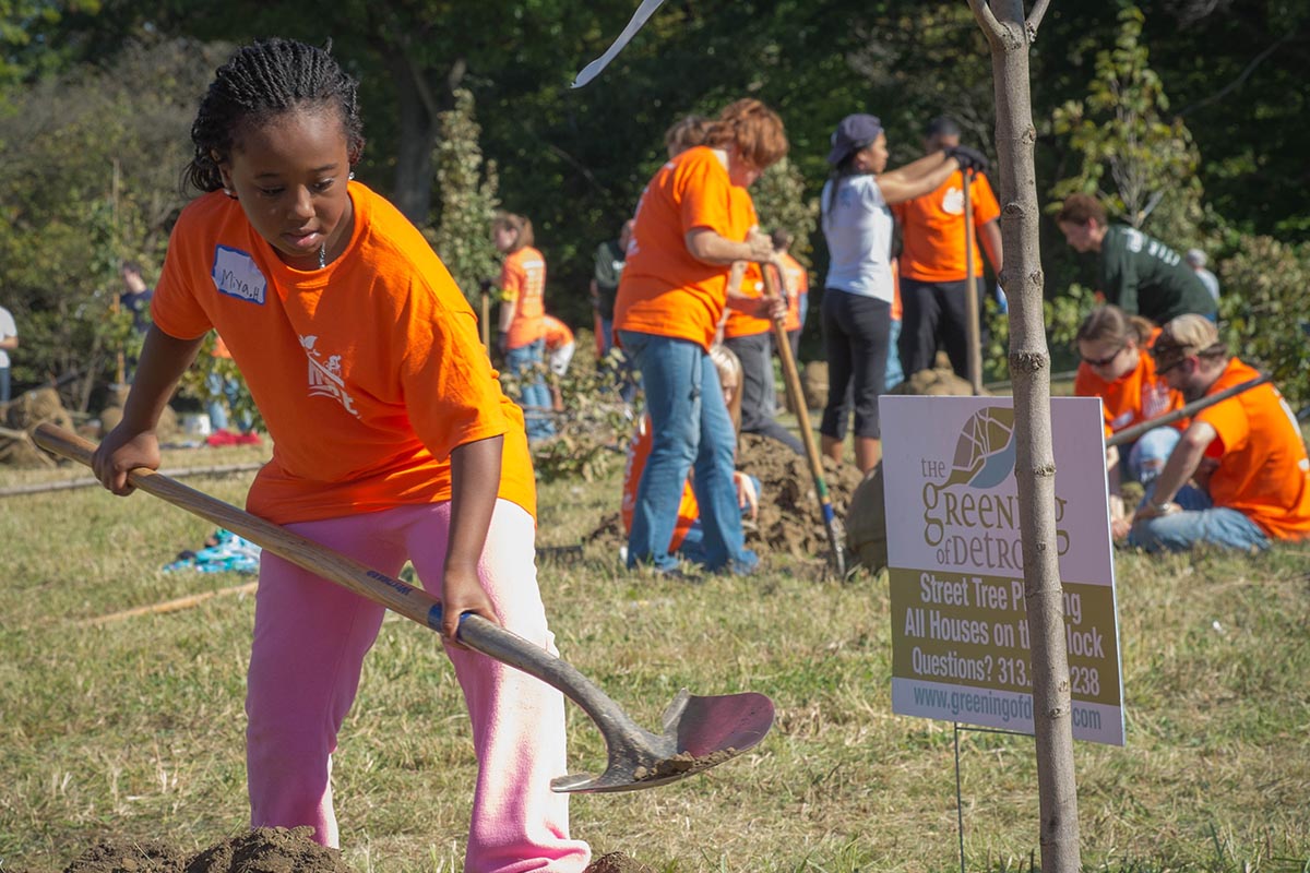 A group of volunteers in orange shirts with shovels, working to plant trees