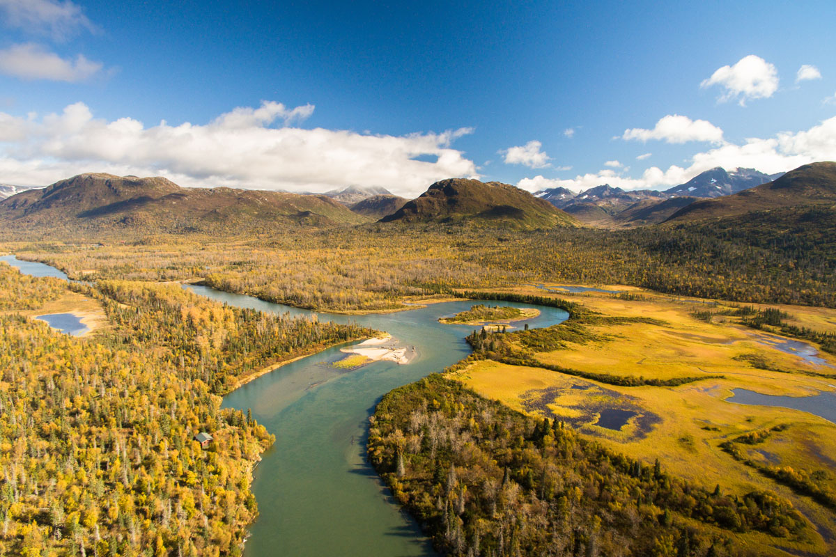 An aerial image of Iliamna River with mountains in the background and clouds low in the sky
