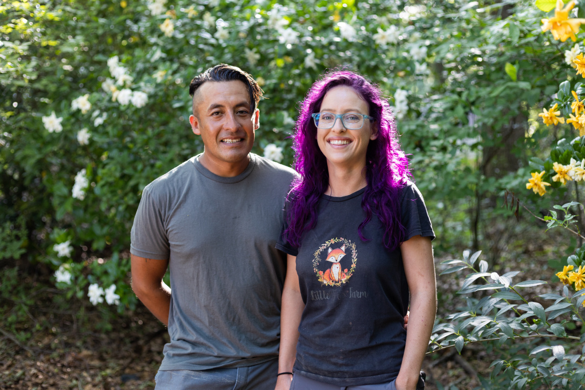 A man and a woman pose in front of green shrubbery