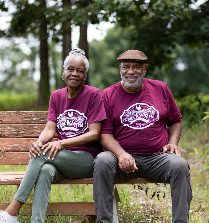 A man and woman sitting on a bench, smiling in a serene outdoor setting.