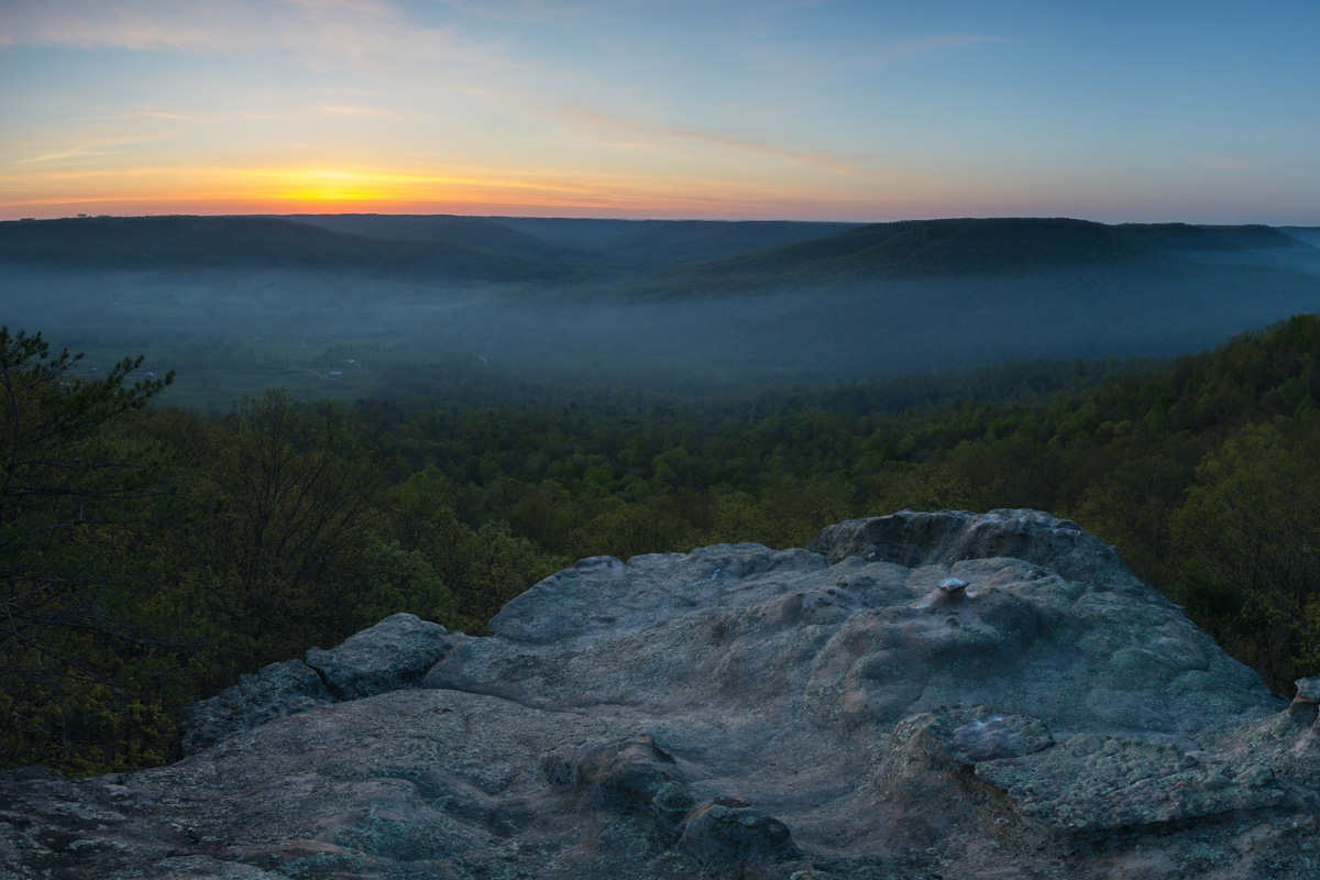 Rock ledge overlooking a forest with mist at sunrise