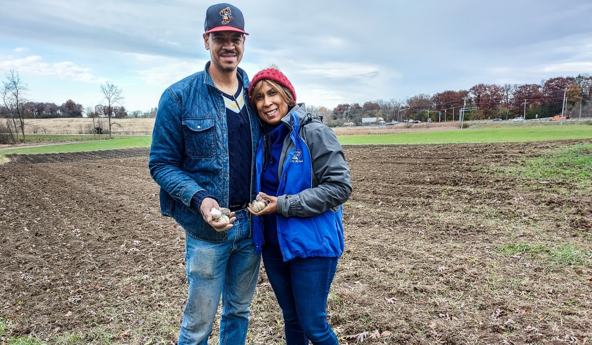 A man and a woman, the owners of Garlic eScape farm, pose on their farmland