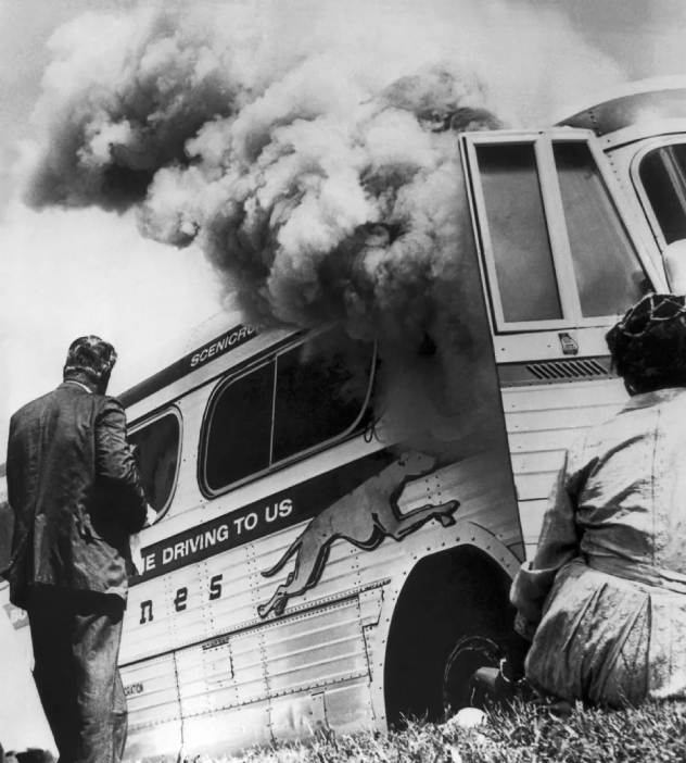 Black and white photo of a man and woman beside a smoking bus, representing Freedom Riders in historical archival footage.