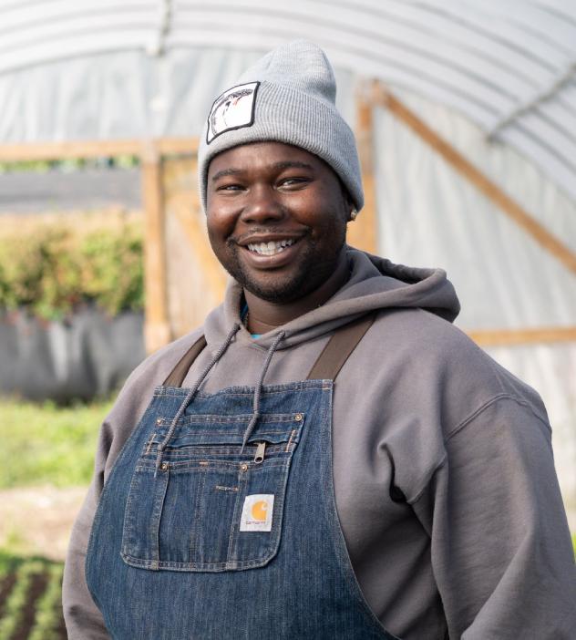 A man in overalls and a hat smiles at the camera, representing the Urban Growers Collective.