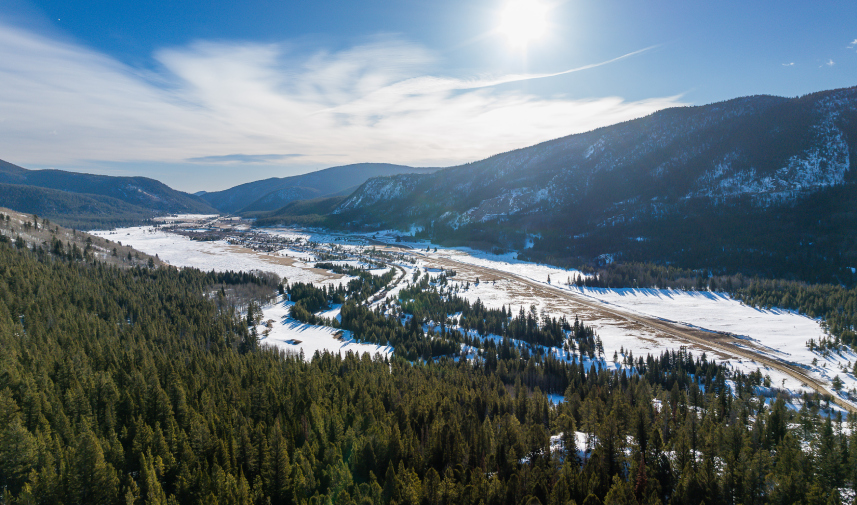 Scenic view of Tolland Ranch with a snowy mountain range, trees, and a river in the background.