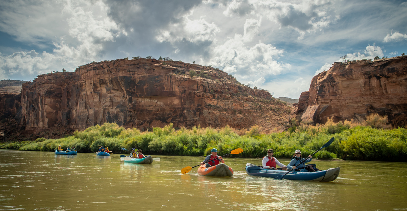 A group of people paddling canoes on a river near Escalante Ranch in Western Colorado, surrounded by lush greenery.