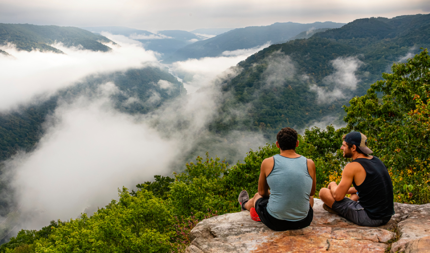 Two men sit on a rock, gazing at the expansive mountains of New River Gorge National Park.