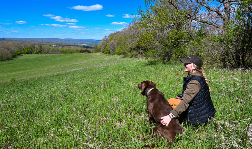 A woman and her dog relax in a field, highlighting the significance of conservation easements for land preservation.