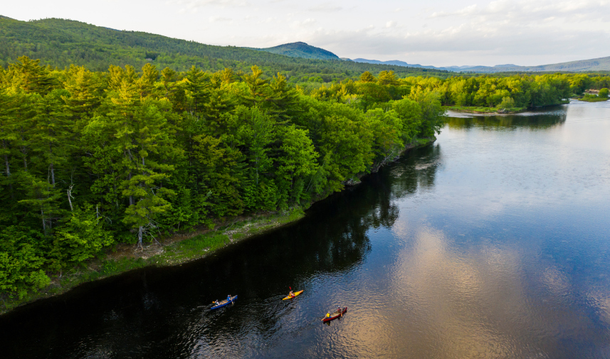 A tranquil river with boats drifting, illustrating the natural beauty preserved through conservation initiatives in Bethel, Maine.